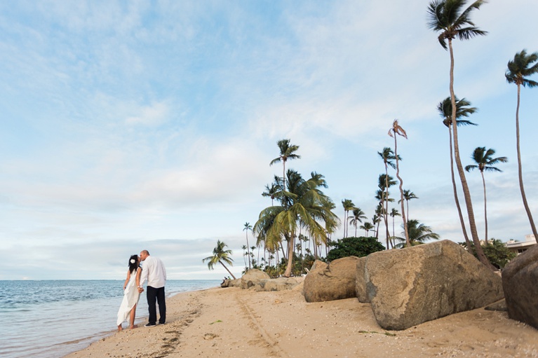 A bride and groom standing on a beach with palm trees.